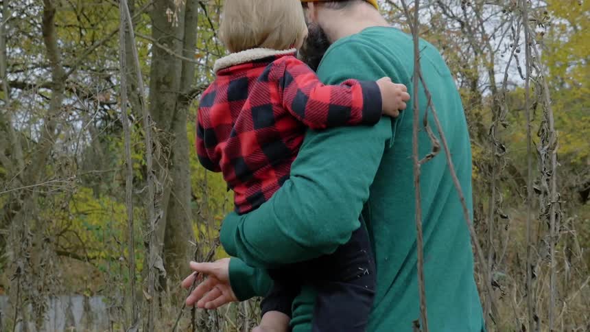 A man carrying a baby walks into the woods