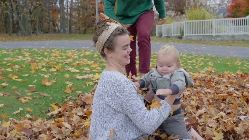 A couple play with babies in a pile of leaves