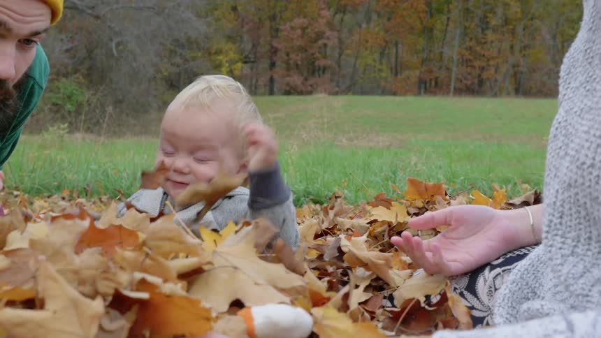 A toddler playing in a pile of leaves with his parents