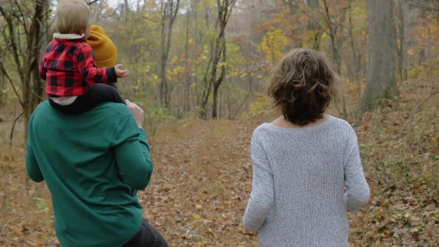 A couple with a baby walk through a forest in autumn