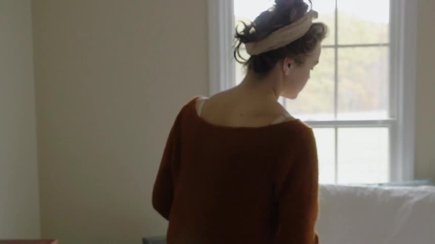 A woman in an orange sweater lies down next to a baby