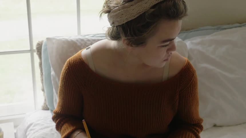 A woman is sitting in bed writing in a book