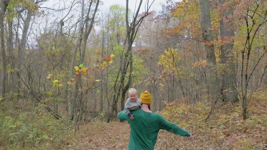 A man is carrying a baby in the woods on his shoulder