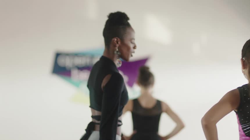 A woman leads students to stretch in a dance class