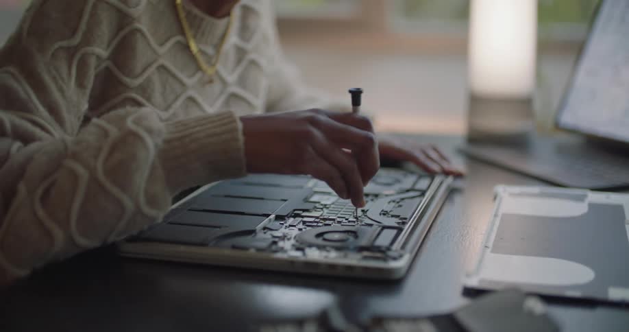 Woman repairs a computer electronic board while reading a schematic on a laptop