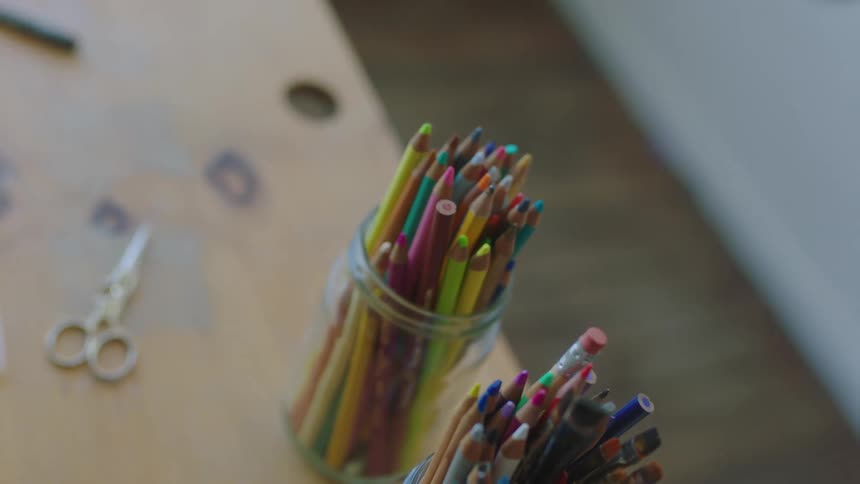A person retrieves a colored pencil from a jar on a table
