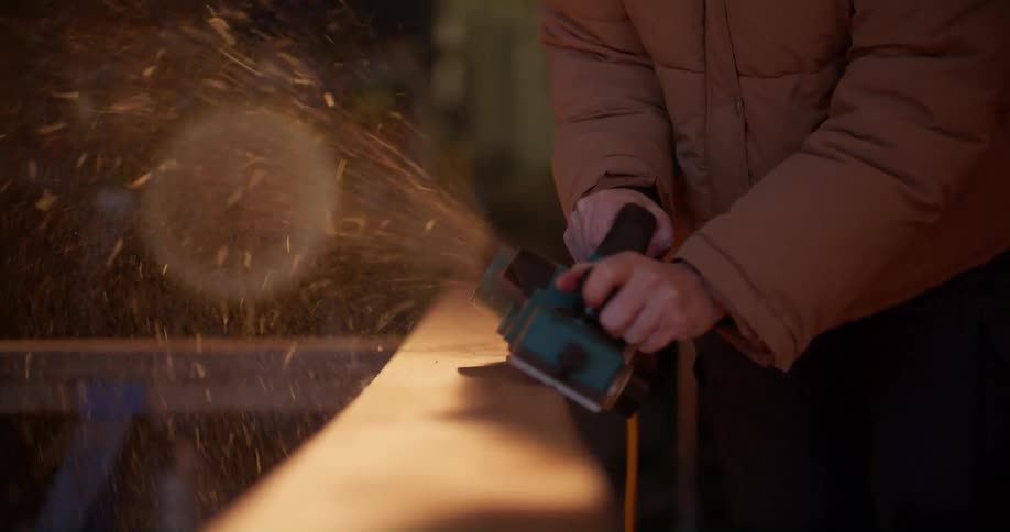 A woman is using a grinder on a large piece of wood in a workshop
