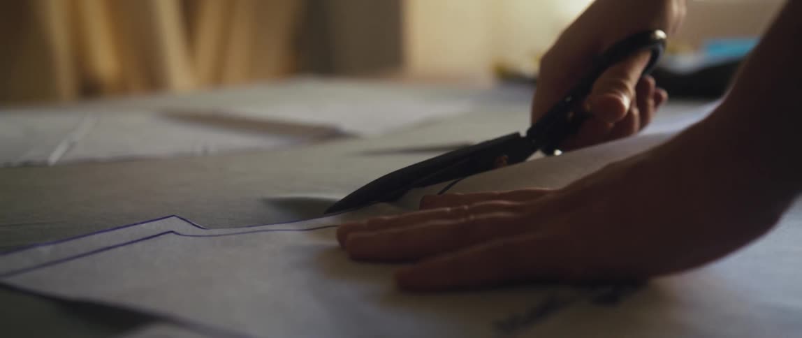 A woman is holding down a pattern with one hand and using scissors to cut it with the other hand