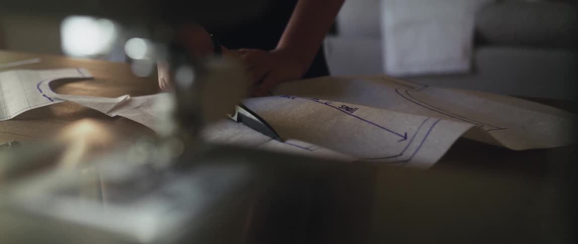 A person uses large scissors to cut along lines drawn on a large sheet of paper on table