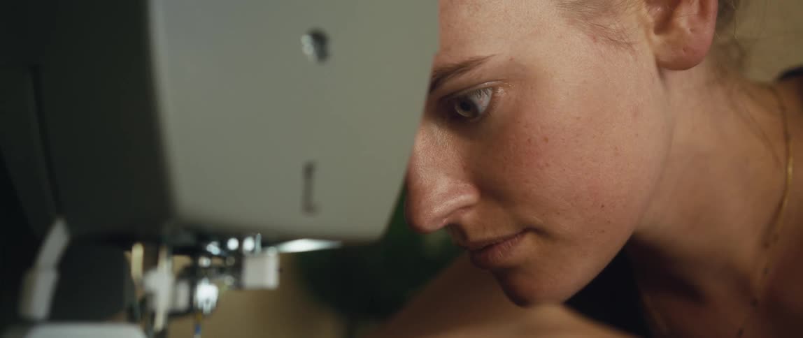 A woman watches closely as she sews with a sewing machine