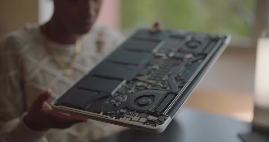A woman has the cover of a laptop removed and is inspecting it
