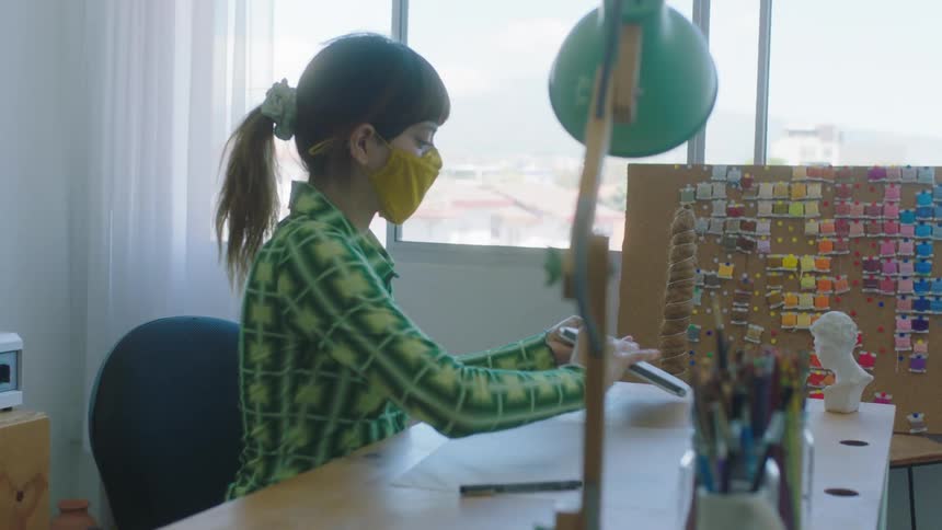 A young woman is sitting by a desk and opening the laptop