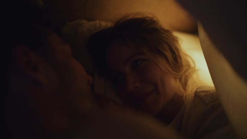 Couple lying in bed under the blanket romantically staring at each other