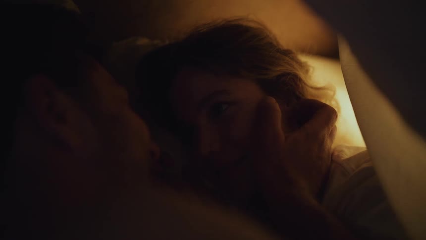 Man caresses womans face then hugs her as they lie on bed