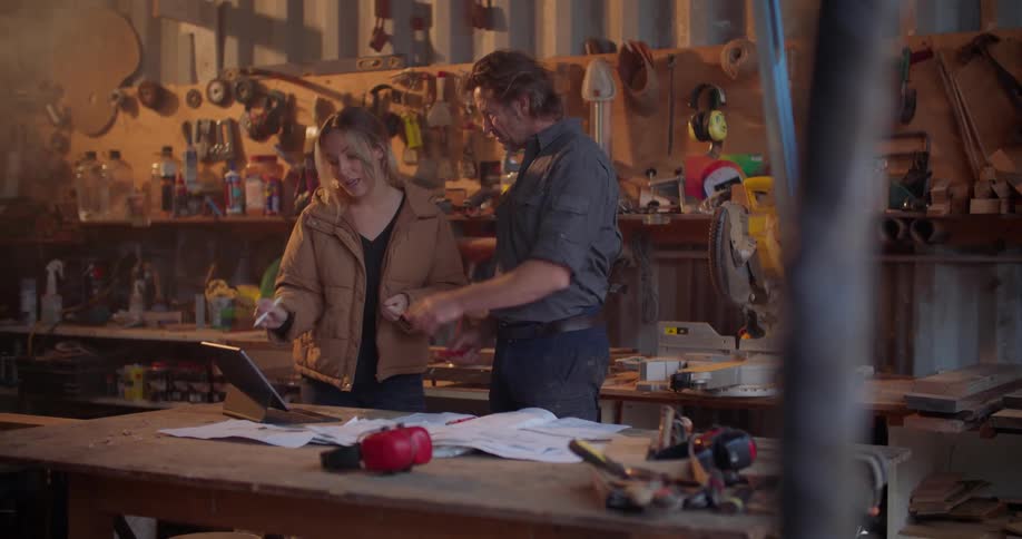 A woman and man talk while referencing a computer tablet resting on its stand on a table in a workshop