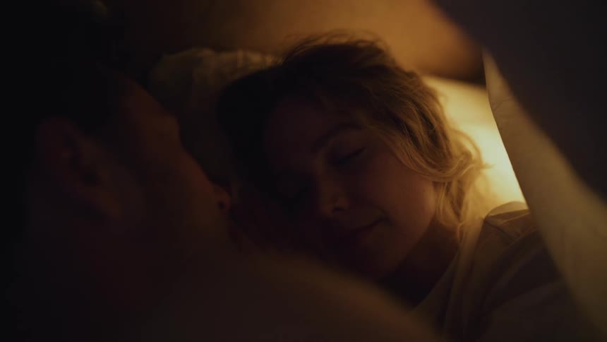 A woman lies in bed and looks at her sleeping husband