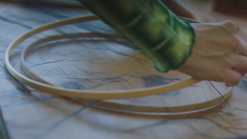 A woman lays fabric between two hoops for embroidery