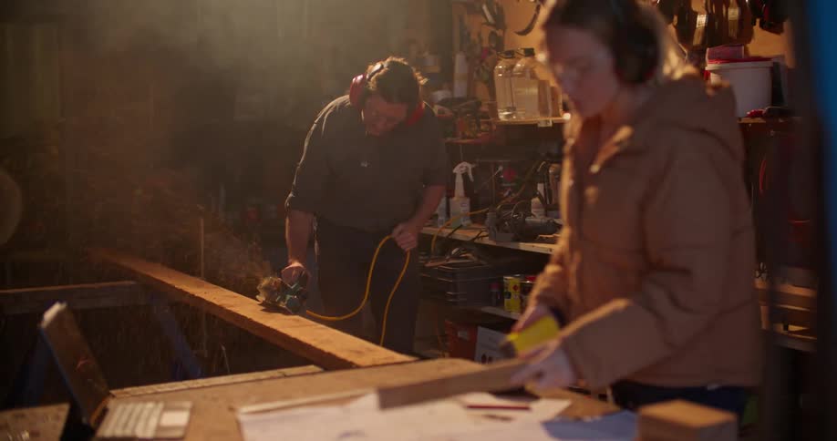 A man and woman working in a workshop both sanding wood