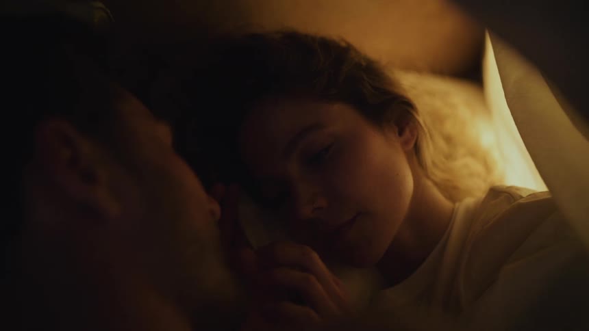 Man and woman lie on bed facing each other