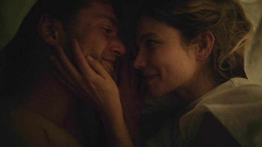 Loving couple lying in bed under a blanket having a conversation while caressing each other