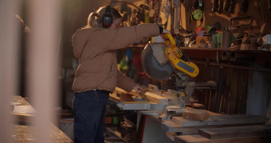 A man is in the background working as a woman measures and cuts a piece of wood