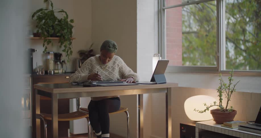 A woman consults her tablet while trying to repair a laptop in her office