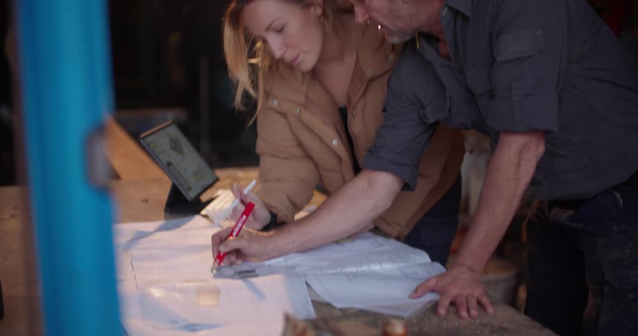 A man and woman talk with each other while looking over designs in a workshop