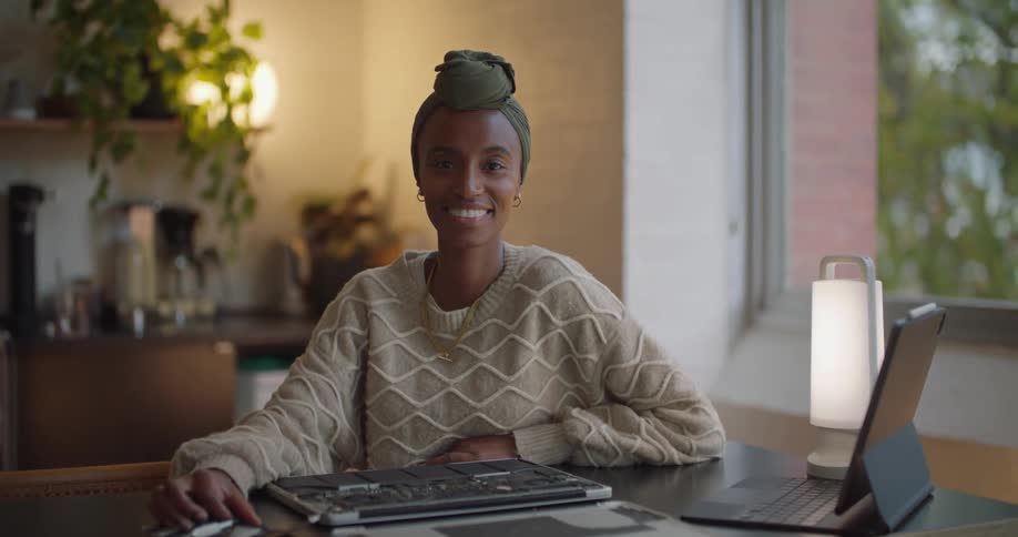 A woman is sitting at a desk and smiling with a laptop that has been taken apart