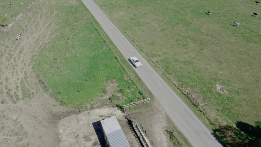 A car travels down a road between farms