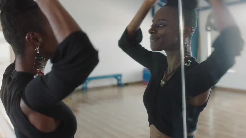 A young smiles while checking her appearance in a full length mirror before resting her back against the mirror and looking into the camera