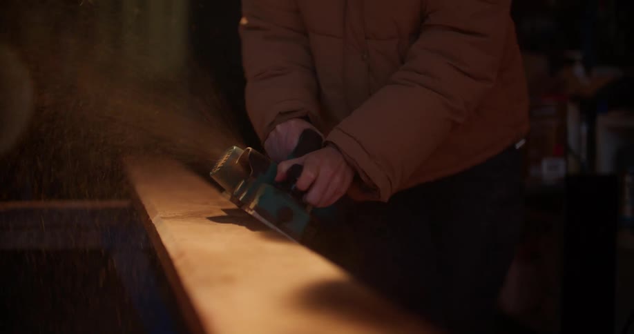 A woman uses a power planer to plane a plank of wood in a workshop