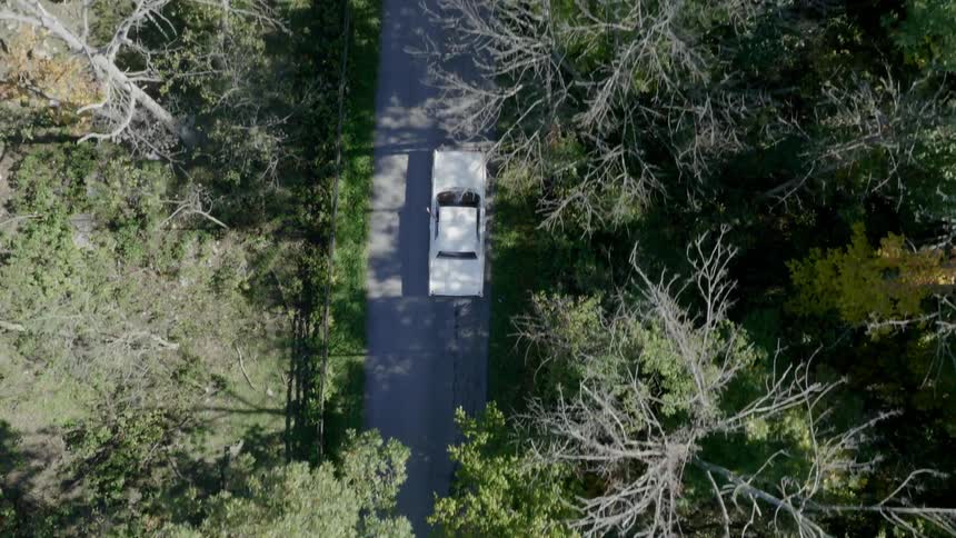 An old car travels through a narrow rural road
