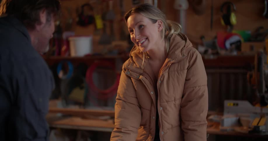 A woman looks at sheets of furniture assembly instructions on a table while talking to a man standing opposite her in workshop