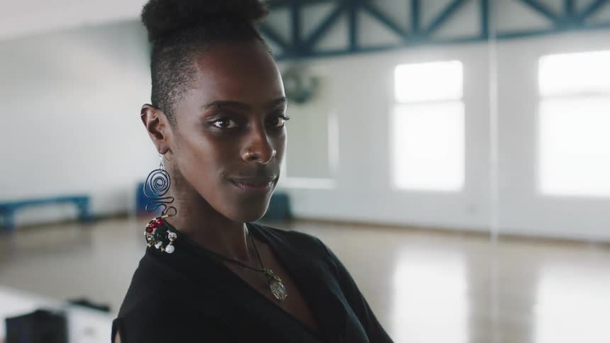 A woman looks into the camera as she walks towards it and strikes a pose