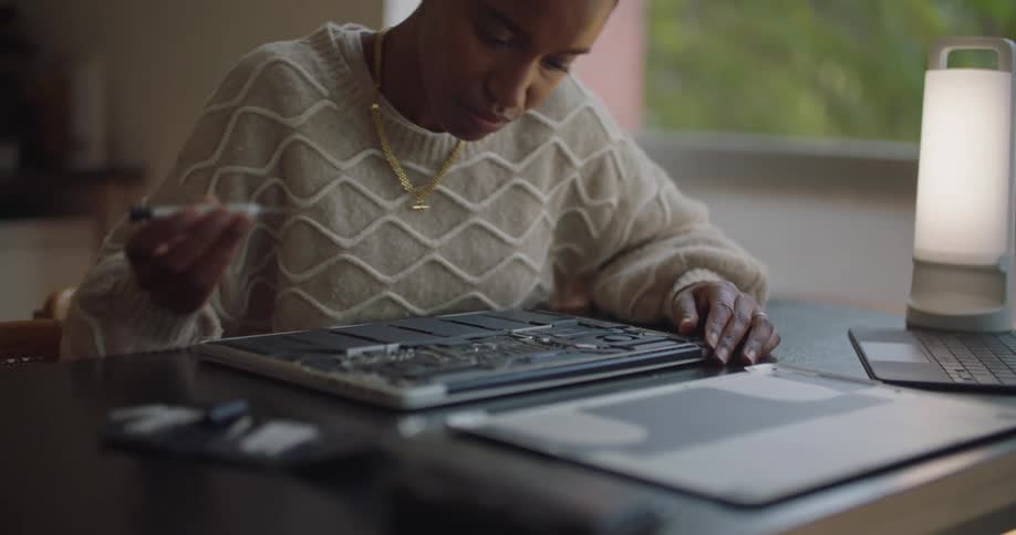 A woman puts a new head on a screwdriver and works on repairing a laptop
