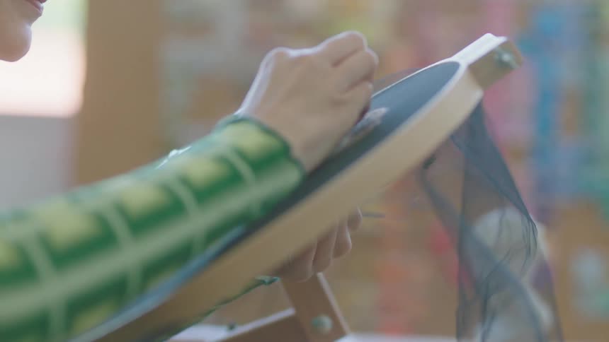 Woman works on embroidery hoop held fabric creating a detailed face
