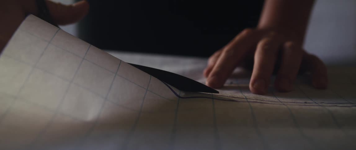 A woman is holding down a pattern with one hand and using scissors to cut it with the other hand
