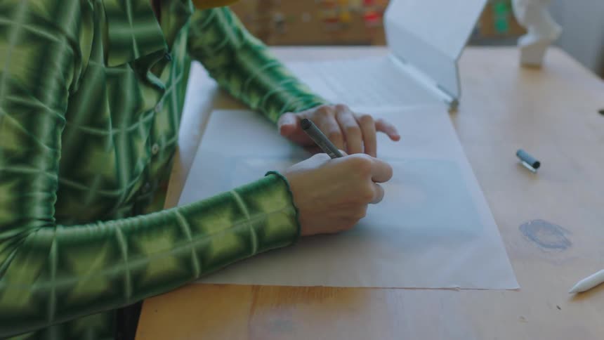 A woman is writing on a piece of a paper by her laptop