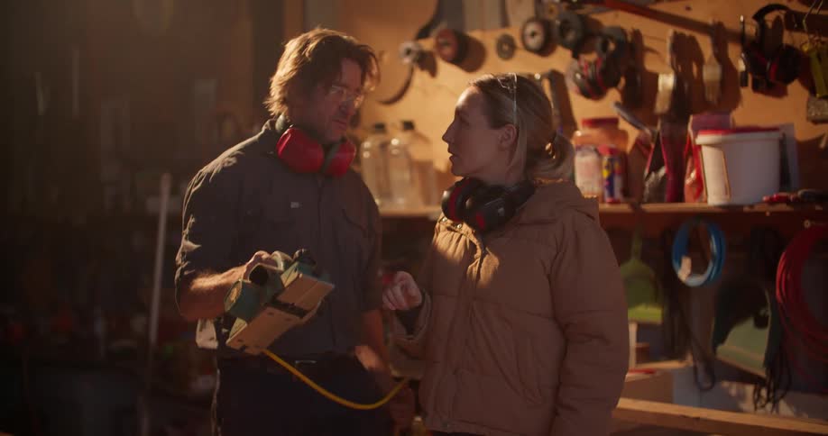 A man explains the operation of a power tool to a woman standing beside him in a workshop