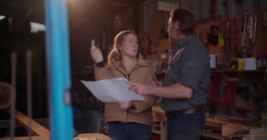 A man and woman talk while reviewing a large document in a workshop during the day