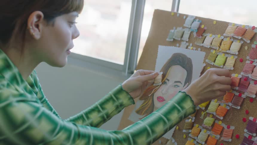 Woman matches colors of embroidery threads to colored sketch of a woman