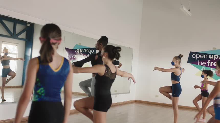 A woman is teaching ballet in a class to a group of young girls