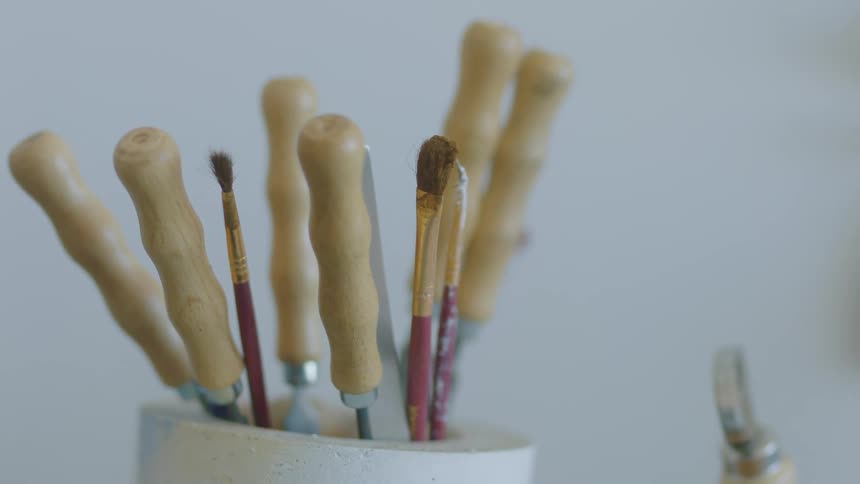 Paint brushes and palette knives stick out of the cup holding them