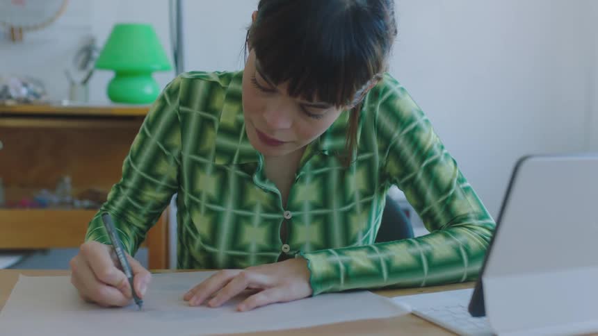 A young woman is sitting by a desk and writing on a piece of paper