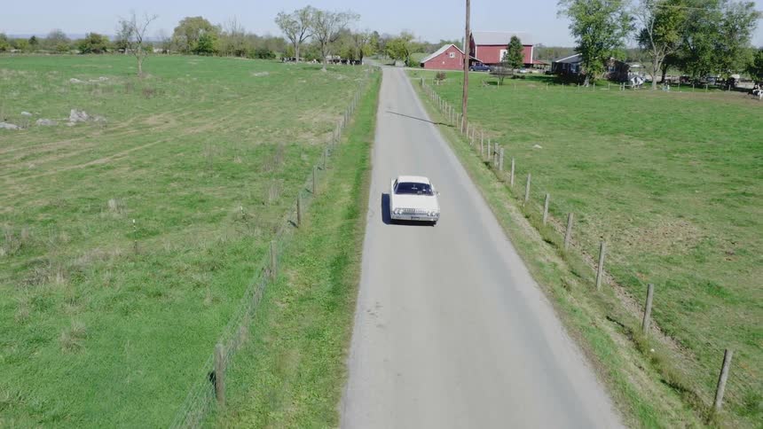 A car rides down a road surrounded by green grass