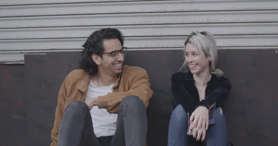 A couple leans against a wall talking and laughing