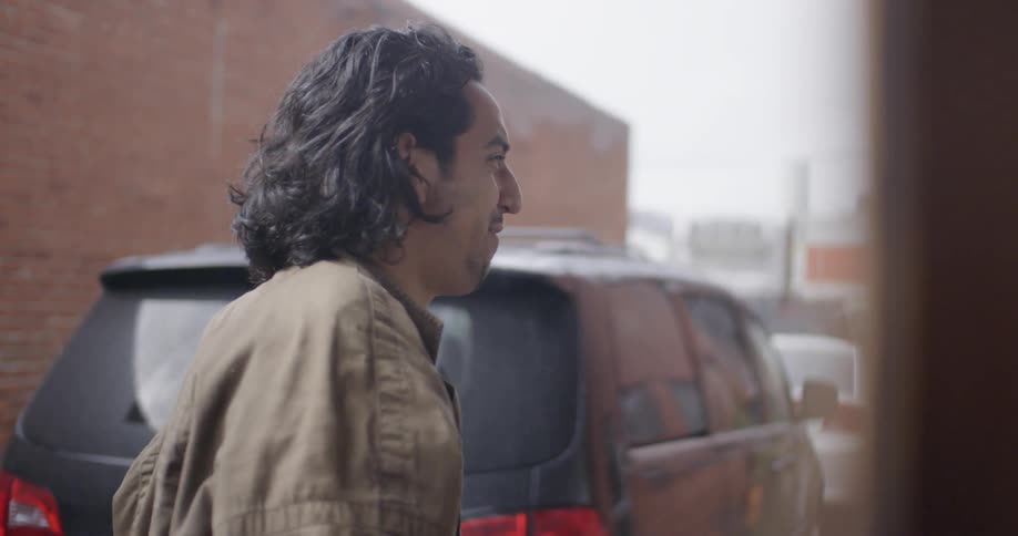 An hispanic man looks down at his camera, speaks, smiles, and then walks away