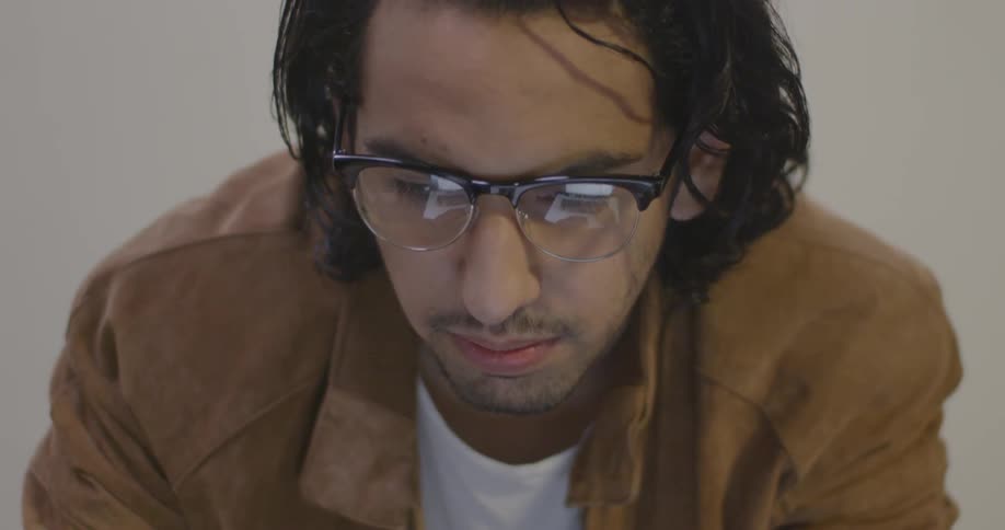 A man wearing glasses looks at something just below him off camera