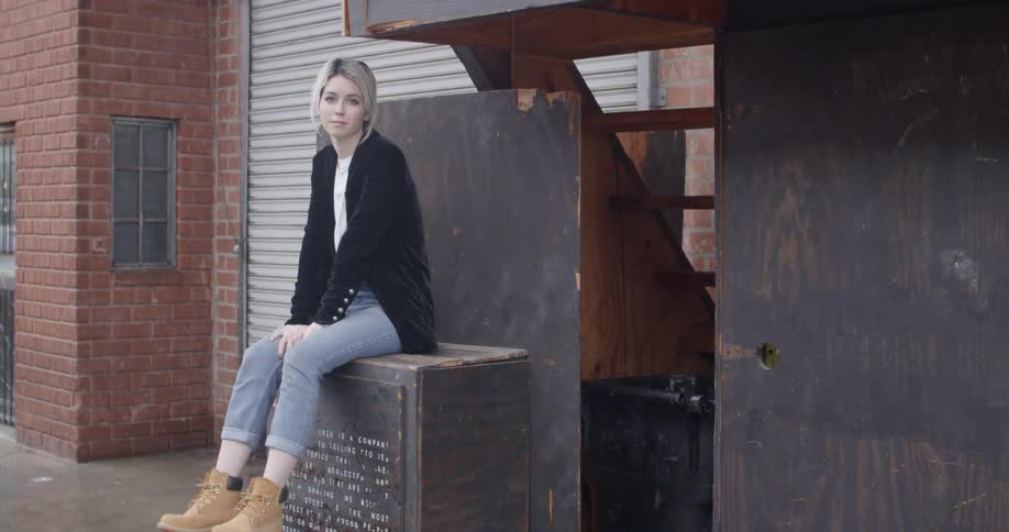 A woman sits on a stone pedestal and swings her legs