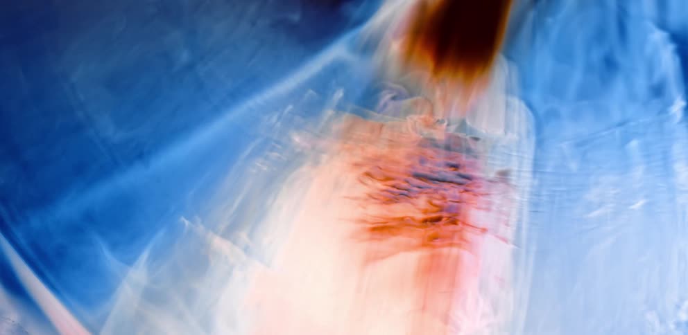Waves of colorful bright blue and maroon smoke floating over a black background
